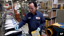 In this May 1, 2012, file photograph, Khan Simom, of Boston, glues cushions to unfinished shoes during the assembly process at the New Balance Athletic Shoe, Inc. factory in Boston. 