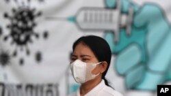 រូបឯកសារ៖ ស្ត្រីម្នាក់ពាក់ម៉ាស់ ដើរកាត់បដាផ្សព្វផ្សាយព័ត៌មានអំពីវ៉ាក់សាំងបង្ការជំងឺកូវីដ១៩ នៅមាត់ទន្លេក្បែរព្រះបរមរាជវាំង ក្នុងរាជធានីភ្នំពេញ កាលពីថ្ងៃទី ១៧ ខែឧសភា ឆ្នាំ ២០២១។