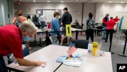 A poll worker wipes down a table as people wait over four hours for early voting at Fairfax County Government Center, Sept. 18, 2020, in Fairfax, Virginia. 