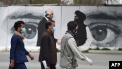 Orang-orang mengenakan masker untuk mencegah penularan Covid-19 melintasi dinding yang dilukis gambar Utusan Khusus AS untuk Rekonsiliasi Afghanistan Zalmay Khalizad (kiri) dan salah satu pendiri Taliban, Mullah Abdul Ghani Baradar (kanan), di Kabul, Afghanistan, 5 April 2020. 