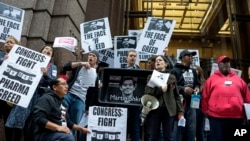FILE - activists hold signs containing the image of Turing Pharmaceuticals CEO Martin Shkreli in front the building that houses Turing's offices, during a protest in New York highlighting pharmaceutical drug pricing, October 1, 2015.
