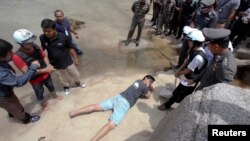 Two workers from Myanmar (wearing helmets and handcuffs), suspected of killing two British tourists on the island of Koh Tao last month, stand near Thai police officers during a re-enactment of the alleged crime, where the bodies of the tourists were foun