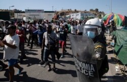 Asylum seekers take part in a rally as riot police block the road near Mytilene town, on the island of Lesbos, Greece, Sept. 11, 2020, after fires destroyed the notoriously overcrowded Moria camp, leaving thousands without shelter.