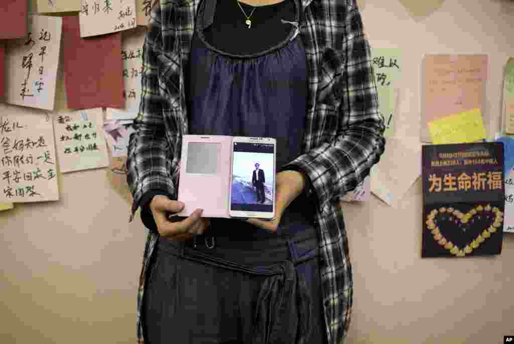 A woman, the daughter of a Chinese passenger on Flight MH370 shows her mobile phone displaying a photo of her father near the wall displaying messages of wishes for the passengers at a hotel in Beijing, April 11, 2014. 