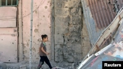 叙利亚南部反政府武装控制的城市德尔萨一个小女孩走过一片废墟。（2017年7月9日）
