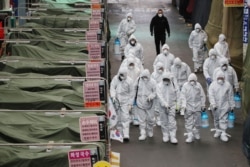 Market workers wearing protective gear spray disinfectant at a market in the southeastern city of Daegu on February 23, 2020 as a preventive measure after the COVID-19 coronavirus outbreak.