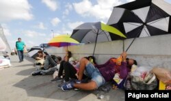 FILE - Immigrants from Guatemala and Cuba seeking asylum in the United States wait on the Matamoros International Bridge, June 28, 2018, in Matamoros, Mexico.