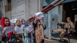 FILE - A Taliban fighter watches as Afghan women hold placards during a demonstration demanding better rights for women in front of the former Ministry of Women Affairs in Kabul, Sept. 19, 2021.