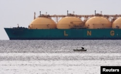 FILE - A fisherman stands in his boat as a liquefied natural gas tanker passes the coast near Havana, Cuba, June 28, 2009.