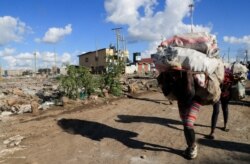 People carry their belongings as they evacuate during riots over the demolition of homes at the Mukuru Kwa Njenga informal settlements in Nairobi, Dec. 27, 2021.