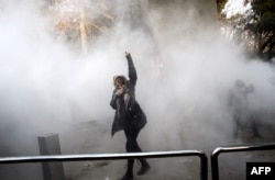 FILE - An Iranian woman raises her fist amid the smoke of tear gas at the University of Tehran during a protest, in Tehran, Iran, Dec. 30, 2017.