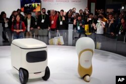 FILE - Attendees wave at Honda robotics concepts 3E-C18, left, and 3E-A18, at CES International, in Las Vegas, Nevada, Jan. 9, 2018.