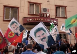 FILE - People hold posters of jailed PKK leader Abdullah Ocalan and PKK flags as they gather outside the headquarters of pro-Kurdish Democratic Regions Party, DBP, on the 17th anniversary of Ocalan’s expulsion from Syria, in Diyarbakir, Turkey, Oct. 9, 2015.