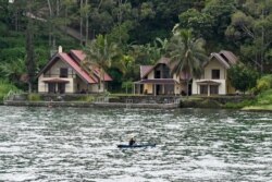 Seorang nelayan mendayung melewati hotel-hotel resor di pulau Samosir, Danau Toba, 3 April 2019. (Foto: dok).
