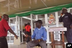 FILE - A health worker takes a man's temperature, center, before his is allowed to enter into a government building, with a message, right, reading "Kindly wash your hands before entering" the building in Monrovia, Liberia, Jan. 14, 2016.