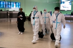 Air China flight crew members in hazmat suits walk through the arrivals area at Los Angeles International Airport in Los Angeles, Nov. 30, 2021.