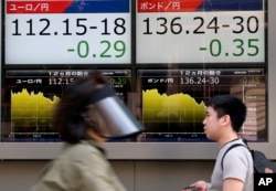 People walk by an electronic board displays exchange rate of euro, left, and British pound at the securities firm in Tokyo on June 27, 2016.