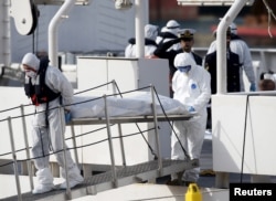 FILE - Italian coast guard personnel in protective clothing carry the body of a dead immigrant off their ship, Bruno Gregoretti, in Senglea, in Valletta's Grand Harbor, Italy, April 20, 2015.