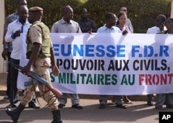 A soldier walks past Malians protesting the junta's arrest of several prominent figures, in front of the hotel where interim president Dioncounda Traore is staying. The sign reads in part, 'Military to the front lines, power to civilians'. Bamako, April 1