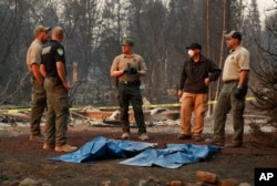 Officials stand over human remains at a burned out home destroyed by the Camp Fire, Nov. 11, 2018, in Paradise, California.