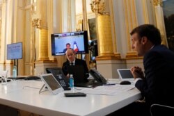 FILE - French President Emmanuel Macron, right, speaks with world leaders while French Foreign Minister Jean-Yves Le Drian listens, during a video conference at the Elysse Palace in Paris, April 24, 2020.