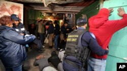FILE - In this photo taken Aug. 17 2018, a policeman searches a suspect during a raid on a known drug house in Mannenburg, Cape Town, South Africa. 