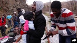 FILE - A migrant from Cameroon helps other migrants on their way to the town of Evzonoi, Greece, Feb. 28, 2015. 