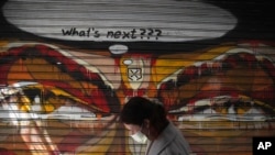 A woman wearing a face mask to protect against coronavirus, passes in front of graffiti painted on the shutter of a closed restaurant during a lockdown order by the Greek government to control the spread of the virus, in Athens, Monday, March 30, 2020.