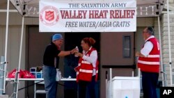 Salvation Army volunteer Francisca Corral, center, gives water to a man at a their Valley Heat Relief Station, Tuesday, July 11, 2023 in Phoenix. (AP Photo/Matt York)