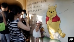 A child poses for photos near a mural depicting Winnie the Pooh in Shanghai, China, Aug. 8, 2018. 