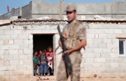 FILE - Locals look on as a Turkish soldier stands guard in a border village on the Turkish-Syrian border near Akcakale in Sanliurfa province, Turkey, Sept. 8, 2019.