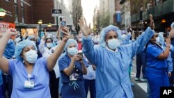FILE - Nurses and medical workers react as police officers and pedestrians cheer them outside Lenox Hill Hospital Wednesday, April 15, 2020, in New York.