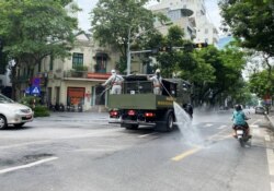 FILE - Men wearing personal protective equipment disinfect a street as the city is under lockdown during a COVID-19 outbreak in Hanoi, Vietnam, July 26, 2021.