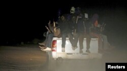 FILE - Migrants sit in the back of a truck as it is driven through a dust road at night in the desert town of Agadez, Niger, May 25, 2015.