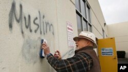 FILE - Tom Garing cleans up racist graffiti painted on the side of a an Islamic center in what officials are calling an apparent hate crime, Feb. 1, 2017, in Roseville, California. The Tarbiya Institute was spray-painted with a dozen obscene and racist slurs. Garing, a retiree who lives in the area and is not a member of the mosque, volunteered to help clean up.