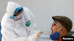 Seorang ahli medis yang mengenakan pakaian pelindung mengumpulkan sampel swab dari seorang pelancong yang telah kembali dari Da Nang, di pusat pengujian cepat COVID-19 di Hanoi, Vietnam, 8 Agustus 2020. (Foto: REUTERS/Kham)