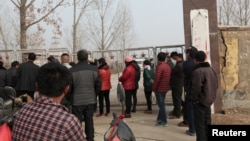 Beberapa warga menunggu di luar komplek tambang gipsum di Pingyi, provinsi Shandong, China yang runtuh hari Jumat (25/12).