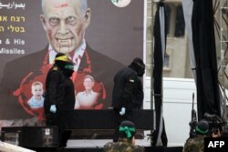 Pejuang Hamas merekam serah terima jenazah empat sandera Israel yang tewas kepada Palang Merah sementara militan lainnya membawa salah satu peti jenazah ke atas panggung di Khan Yunis di Gaza selatan pada 20 Februari 2025. (Eyad BABA / AFP)