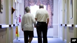 FILE - An elderly woman with Alzheimer's disease is accompanied on a walk down the hall at The Easton Home in Easton, Pennsylvania, Nov. 6, 2015.