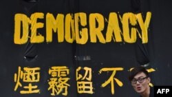 FILE - A pro-democracy protester stands next to a banner in Hong Kong, Sept. 30, 2014. 