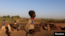 FILE - A brick maker from Ad-Damazin carries a mould of mud bricks to be dried at an open-air factory on Tuti Island, Khartoum, Sudan, Feb. 14, 2020.