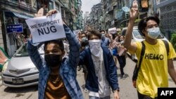 បាតុករ​ម្នាក់កាន់​ស្លាកសញ្ញា​គាំទ្រ​រដ្ឋាភិបាល​រួបរួម​ជាតិ ខណៈ​ដែល​អ្នក​ខ្លះ​ទៀត​លើក​ម្រាម​ដៃ​បី​ជា​សញ្ញា​គាំទ្រ​ដល់​ការ​តវ៉ា​ប្រឆាំង​នឹង​រដ្ឋាភិបាល​យោធា​​ ទីក្រុង​រ៉ង់ហ្គូន ប្រទេស​មីយ៉ាន់ម៉ា ថ្ងៃទី២៧ ខែមេសា ឆ្នាំ២០២១។