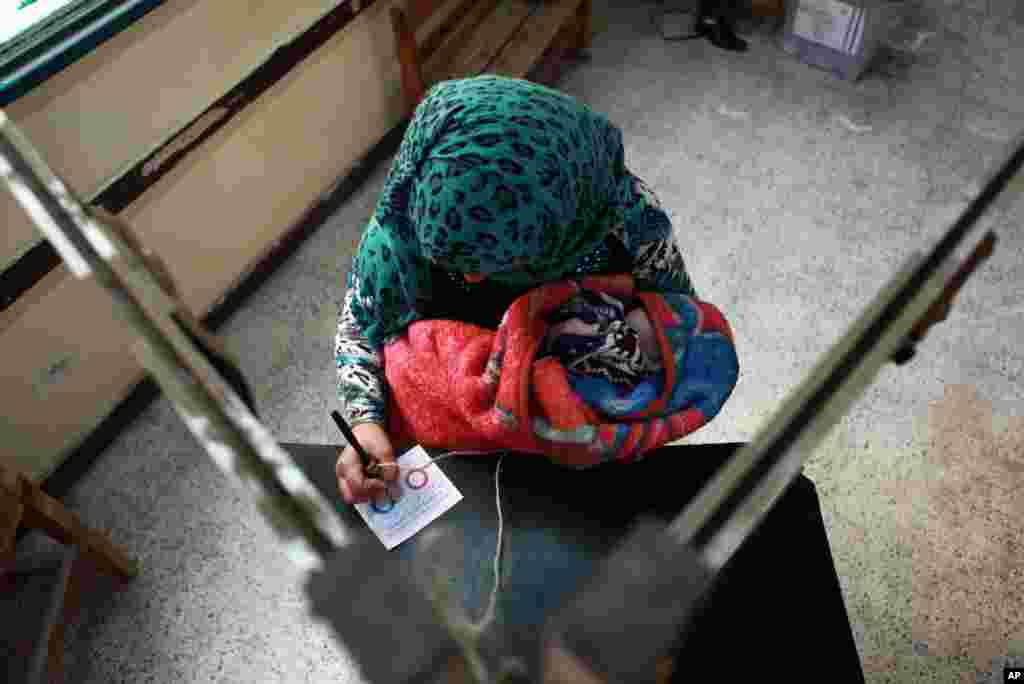 Seorang perempuan menggendok anak saat memberikan suara dalam referendum di Hawamdaya, sebelah selatan Kairo (14/1). (AP/Surat Kabar El Shorouk, Sabry Khaled)