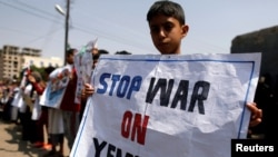 也门首都萨那，一名男孩在联合国办公室外举着标语牌，谴责空袭行动。(2018年8月13日)