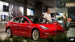 FILE- In this July 6, 2018, file photo, a prospective customer confer with sales associate as a Model 3 sits on display in a Tesla showroom in the Cherry Creek Mall in Denver.