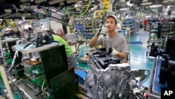 In this Aug. 2, 2017, photo, Nissan Motor Co. factory workers check engines on an assembly line at its plant in Yokohama, near Tokyo.