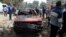People stand near a damaged car after explosions near Cairo University, April 2, 2014. 