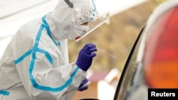 A medical staff member wearing a protective suit takes a swab sample of a person at a newly opened drive-in sampling station in Prague, Czech Republic, Oct. 7, 2020. 