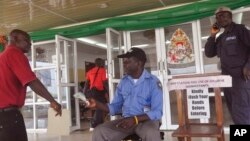 Un homme se fait prélever la température d’être autorisé à entrer dans un bâtiment du gouvernement, où un message, à droite, indique "veuillez laver vos mains avant d'entrer dans" le bâtiment à Monrovia, Libéria, le 14 janvier 2016. 