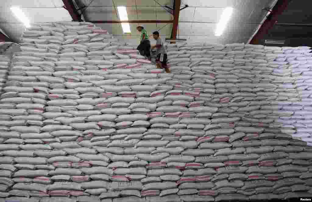 Dua orang pekerja berjalan di tumpukan beras di sebuah gudang beras milik pemerintah Filipina di distrik Taguig, Manila, Filipina.&nbsp;